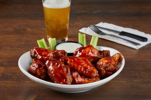 a plate of chicken wings, celery with a beer on the side