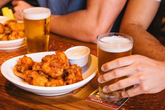 a plate of wings and dipping sauce and someone grasping a beer